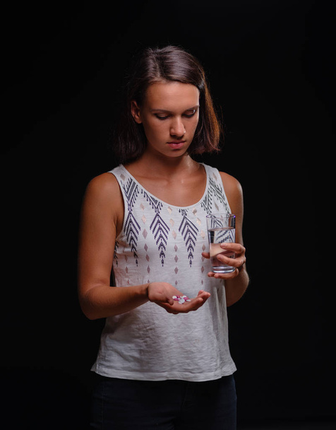 Portrait of a female patient on the black background. Girl with water and prescripted meds. Pharmaceutical help concept. - Photo, image