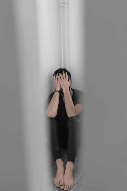 Nuori mies tuskissaan istuu tyhjässä huoneessa
 - Valokuva, kuva