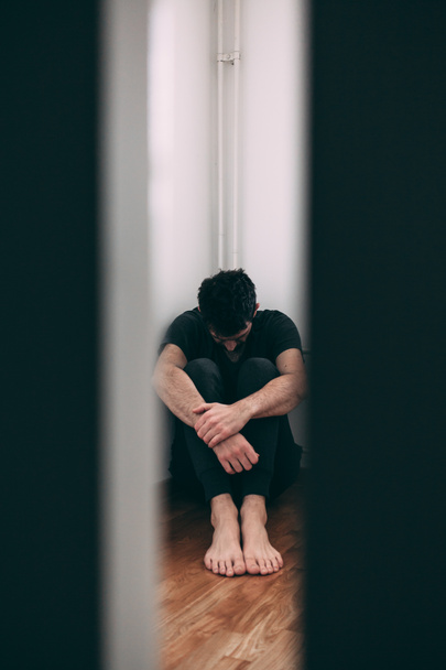 Jeune homme dans la douleur assis dans la chambre vide
 - Photo, image