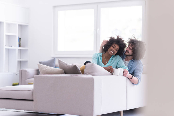 multiethnic couple sitting on sofa at home drinking coffe - Photo, Image