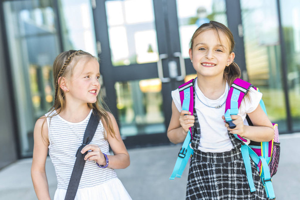 Due ragazze fuori dalla scuola con le borse del libro
 - Foto, immagini