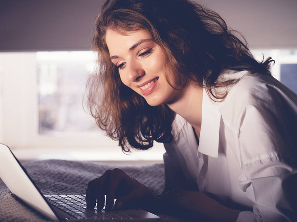 Beautiful young woman lying on the bed with notebook - Foto, afbeelding