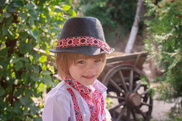 Portret van een jongetje in een wit geborduurd overhemd en een hoed - Foto, afbeelding