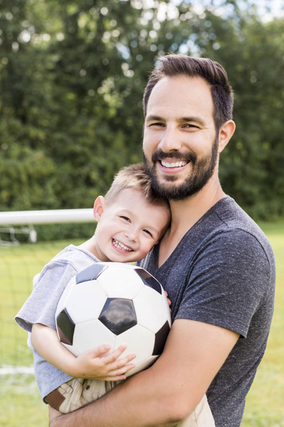 Młody ojciec z synkiem grający w piłkę nożną na boisku - Zdjęcie, obraz