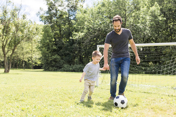 Young father with his little son playing football on football pitch - Фото, зображення