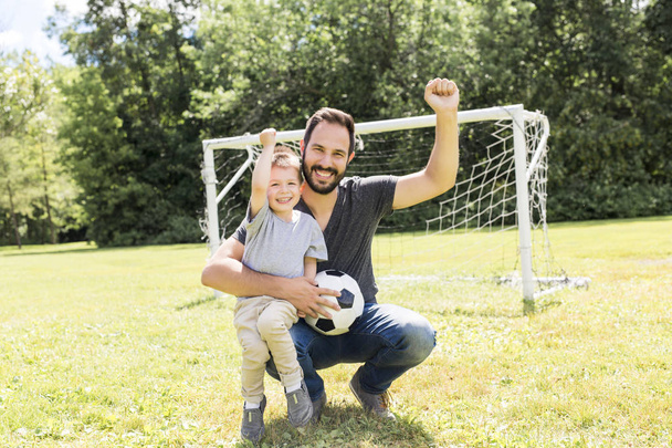 Genç baba ve küçük oğlu futbol sahasında futbol oynuyor. - Fotoğraf, Görsel