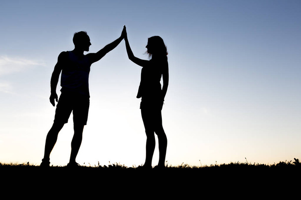 Happy silhouette couple holding up hands against the sky at dusk - 写真・画像