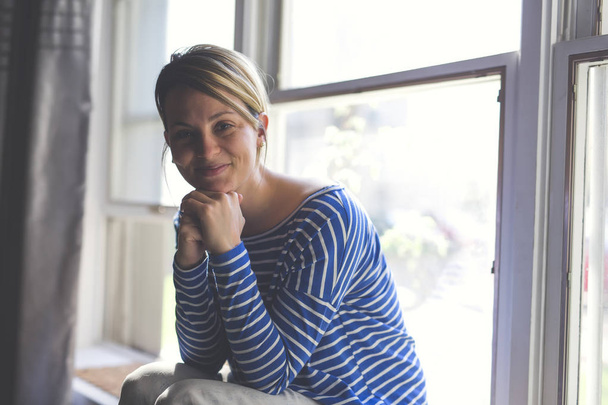 Beautiful young woman sitting near window - Φωτογραφία, εικόνα