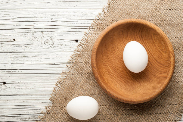 chicken eggs in wooden plate on white wooden background - Fotó, kép
