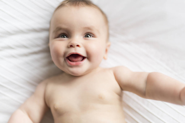 Cute happy 7 month baby girl in diaper lying and playing - Φωτογραφία, εικόνα