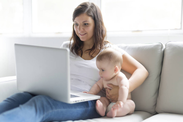 mother and baby child are looking to play and read computer on the couch at home - Foto, Bild