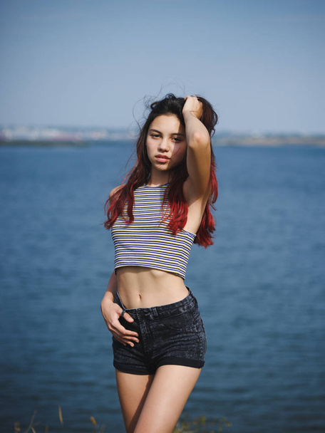 Sexy, cute young girl touching her hair. A teenager on a blurred river background. Beauty and style concept. Copy space. - Foto, imagen