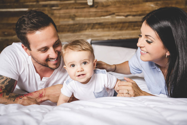 Loving parents with their cute little boy on bed - Foto, afbeelding