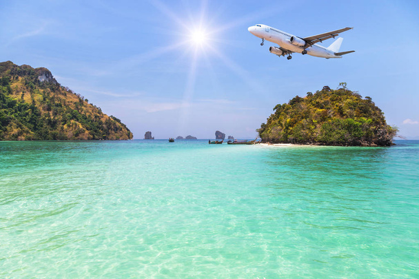      passenger airplane landing above small island in blue sea and tropical beach on blue sky with sunlight.  - Photo, Image