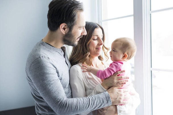 portrait of young family relaxing close to the window with baby - Foto, imagen