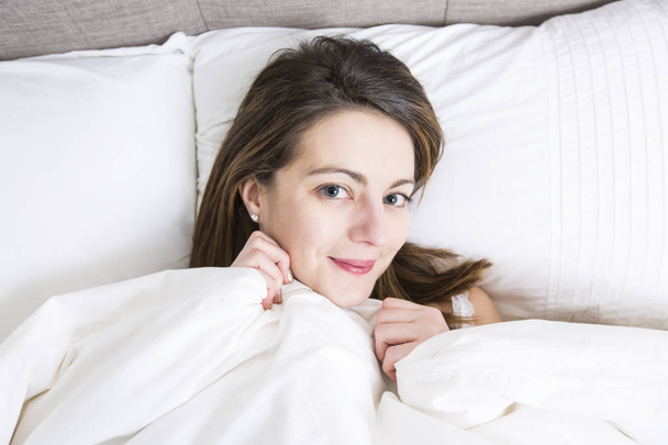 Mujer joven durmiendo en el dormitorio en casa vistiendo de blanco
 - Foto, imagen