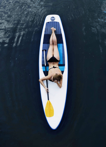 Attractive woman in bikini is sunbathing on a surfboard, aerial view - Photo, image