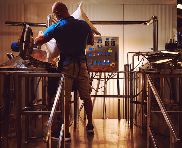 Brewer in brewhouse pouring out the malt to the tank - 写真・画像