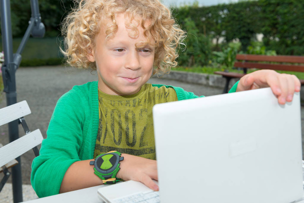 pequeño niño rubio usando un ordenador portátil, al aire libre
 - Foto, imagen