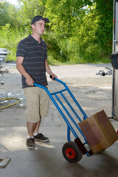 mladý zaměstnanec nese balíček s handtruck - Fotografie, Obrázek
