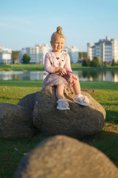 Little girl sitting on stone in sunset - Foto, imagen