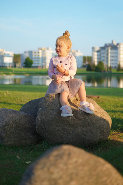 Little girl sitting on stone in sunset - Photo, Image