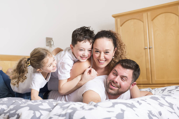 οικογένεια, παιδιά και σπίτι έννοια - ευτυχισμένη οικογένεια με δύο παιδιά κάτω από την κουβέρτα στο σπίτι - Φωτογραφία, εικόνα