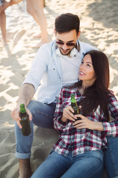 Happy couple smiling and drinking beer at beach - 写真・画像