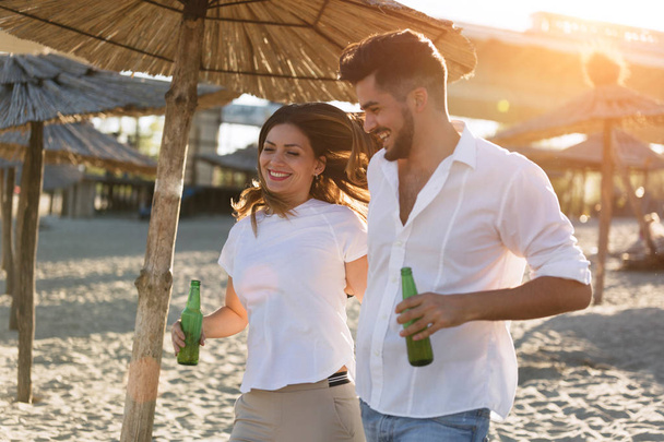 Szczęśliwa para uśmiechając się i pije piwo na plaży - Zdjęcie, obraz