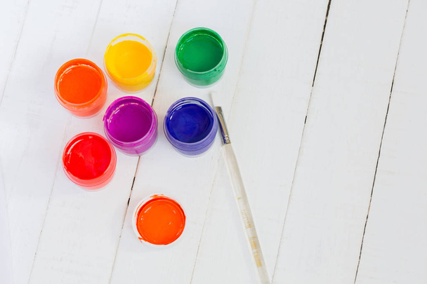 Open jars with colorful paint and transparent clean brush on a white wooden background - Photo, Image