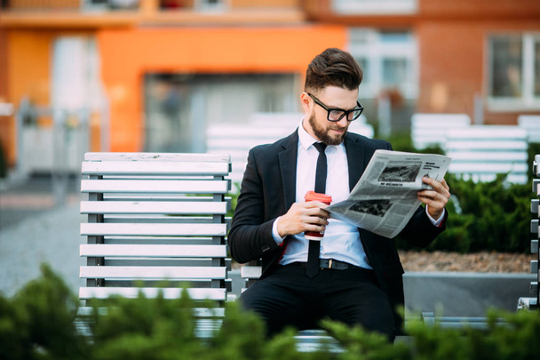 Uomo d'affari premuroso con giornale e tazza di caffè seduto sulla panchina
 - Foto, immagini