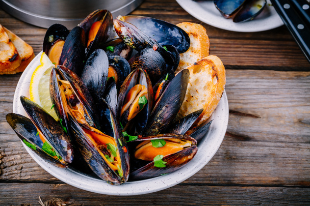 Delicious seafood mussels with with sauce and parsley.  Lemon and baguette . Clams in the shells.   - Photo, Image