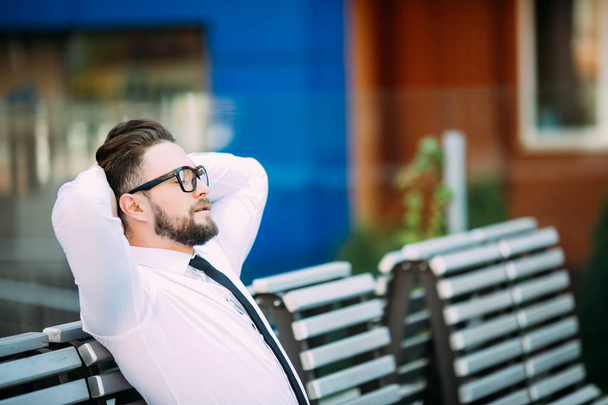 Homem de negócios relaxado sentado em um banco com as mãos sobre a cabeça e desfrutar de tempo livre após o sucesso
 - Foto, Imagem