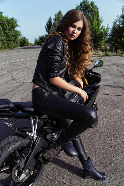 young woman in leather clothes near a motorcycle - Фото, изображение