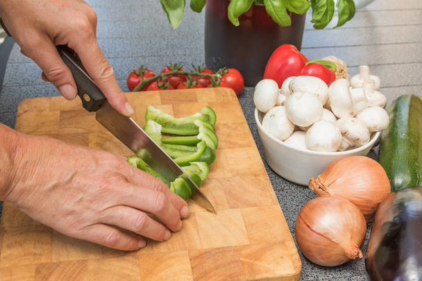 Side view of woman slicing a green paprika on a wooden board - Foto, Bild
