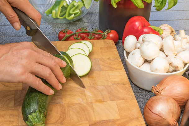 Side view of woman slicing a zucchini on a wooden board - Photo, Image