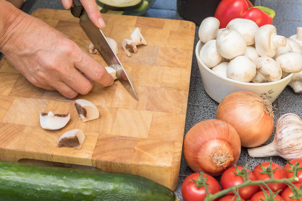 Side view of woman slicing a mushrooms on a wooden board - Photo, image