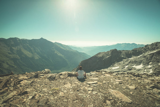 Une personne assise sur un terrain rocheux et regardant un lever de soleil coloré dans les Alpes. Vue grand angle d'en haut avec des sommets de montagne lumineux en arrière-plan. Image tonique
. - Photo, image