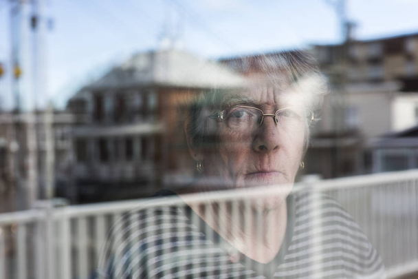 Senior mulher olhando através de uma janela como deprimir
 - Foto, Imagem