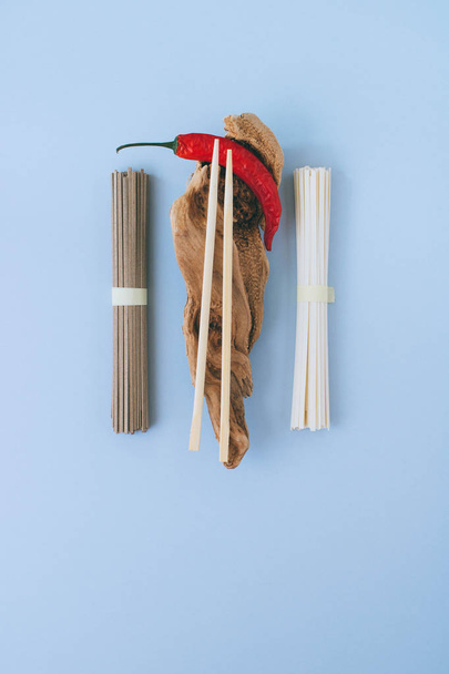 Asian noodles udon and soba, red chili, chopsticks on wooden sticks on a bright blue background. Minimalism. Flat lay. - Foto, afbeelding
