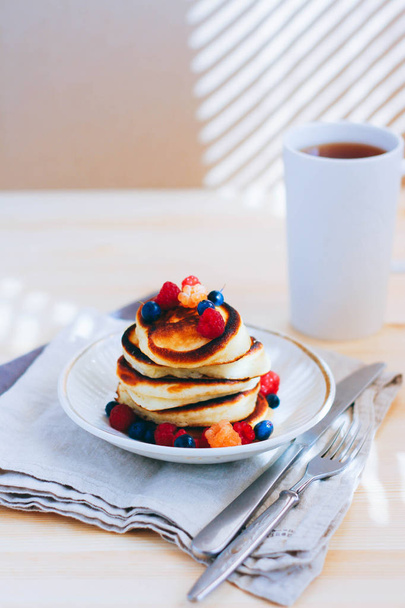 Café da manhã, panquecas exuberantes com frutas frescas, framboesas e mirtilos e uma xícara de chá
 - Foto, Imagem