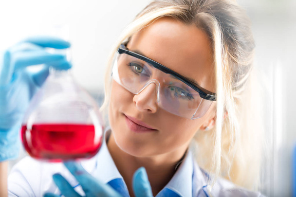 Young attractive female scientist holding a flask with blue liqu - Фото, изображение