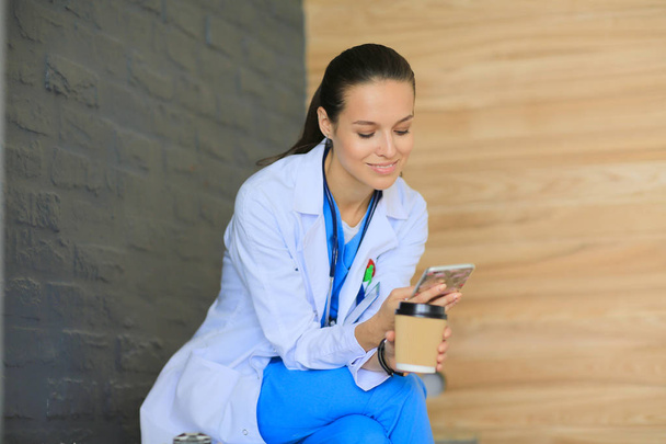 Young woman doctor sitting with your phone. Woman doctors. - Фото, изображение