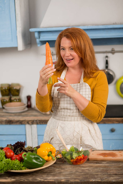 Housewife in the kitchen holding huge carrot. - Valokuva, kuva