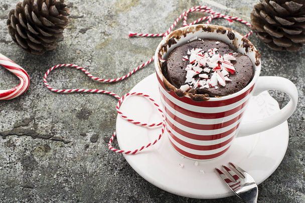 A mug cake for a festive New Year's Eve snack with red white sweets in a striped red white mug on a gray stone background with winter paraphernalia. Selective focus. - Фото, изображение