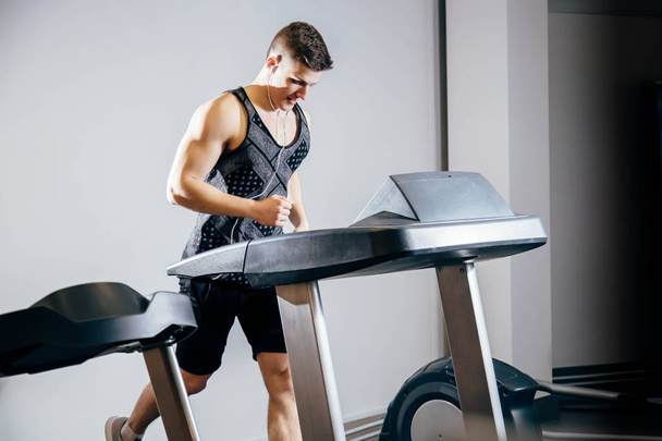 Handsome man with earphones running on treadmill in sports club - Foto, afbeelding