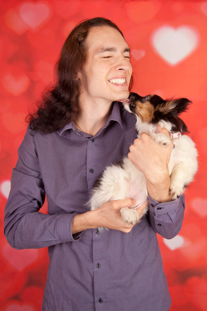 гарний усміхнений щасливий чоловік з 3-місячним цуценям-папіоном. молодий хлопчик і собака найкращі друзі
. - Фото, зображення