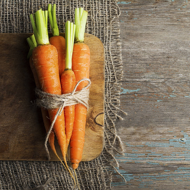 A bunch of fresh juicy young carrots are tied with string on a simple wooden background with burlap. Top View. - Fotografie, Obrázek
