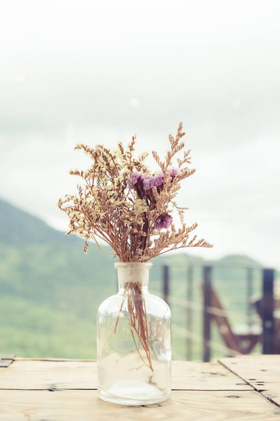 Букет высохших цветов в стеклянной вазе на деревянном столе.. - Фото, изображение