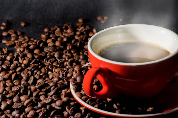 Ζεστό καφέ στο φλιτζάνι κόκκινο και κόκκους καφέ αποτελούν το υπόβαθρο. - Φωτογραφία, εικόνα